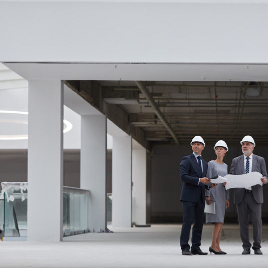 Three people in suits and hard hats standing inside a building.