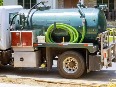 A green truck with a hose attached to the back of it.