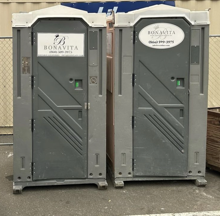 Two portable toilets are standing in a parking lot.