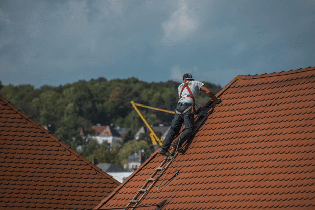 Construction worker on a steep roof installing new shingles under sunny skies