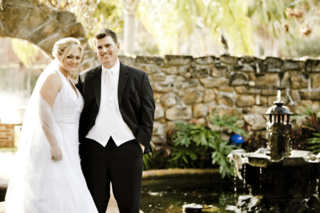 Bride and groom standing by a stone fountain at an outdoor wedding.