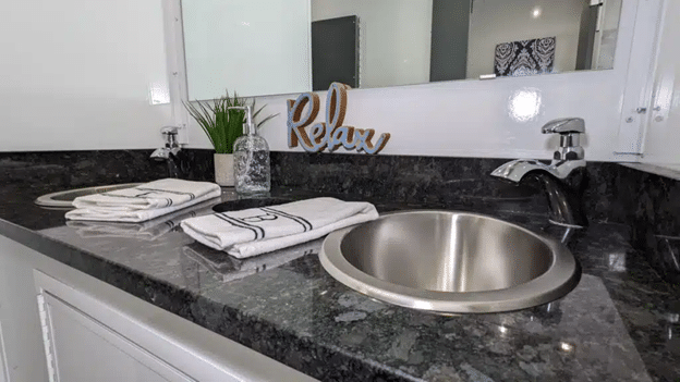 Luxury restroom trailer vanity with granite countertop, dual stainless sinks, towels, and décor.