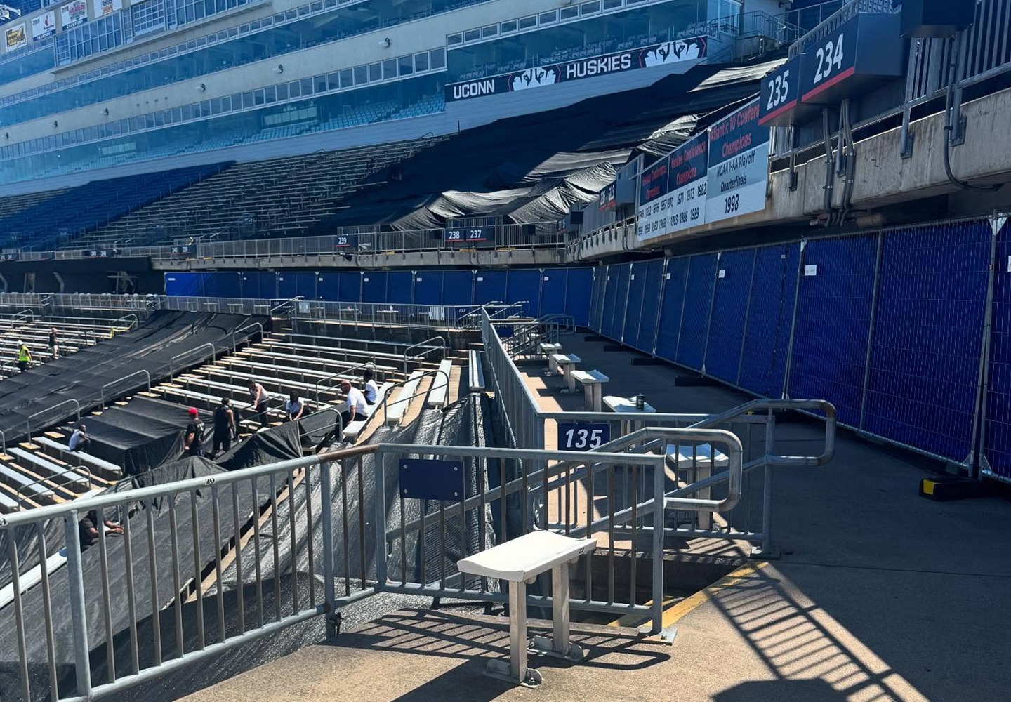 Stadium concourse lined with blue screened fence panels during seating renovations.