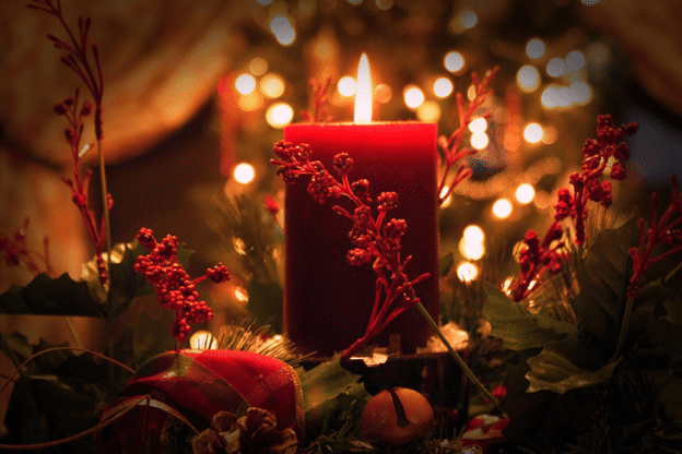 Red pillar candle glowing in a holiday centerpiece of greenery and berries.