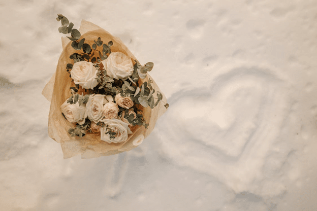 Bridal bouquet on snow beside a heart shape drawn in the drift.