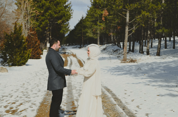Couple holding hands on a snowy forest road lined with pines.