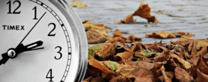 Time for Fall events is closer that you think. Close-up clock beside fallen autumn leaves on wet pavement.
