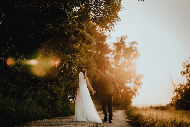 Bride and groom walking hand in hand down a country lane at sunset.