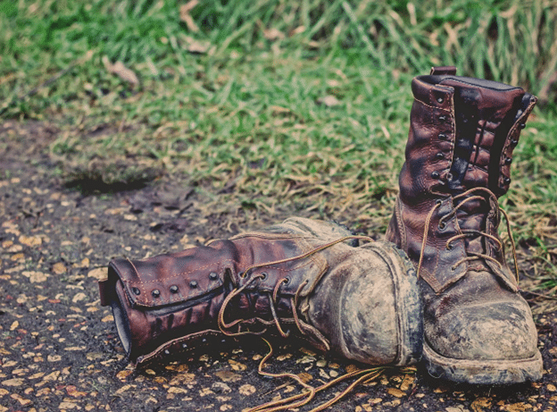 Pair of muddy work boots on a gravel path beside grass.