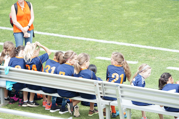 Youth girls soccer team seated on the sideline bench.