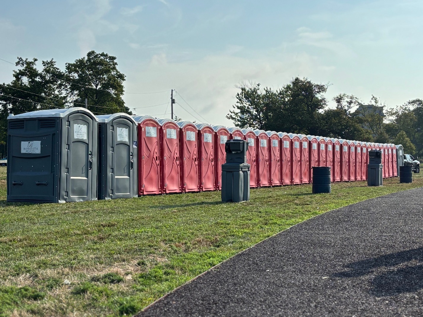 Long row of portable restrooms with handwash stations set up for an outdoor event.
