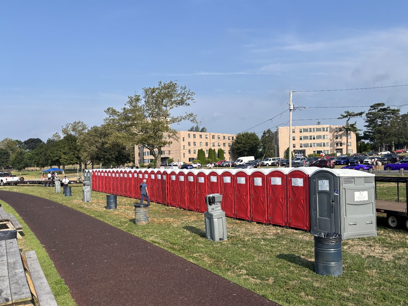 Long row of red portable restrooms with ADA unit and handwash stations at an outdoor event.