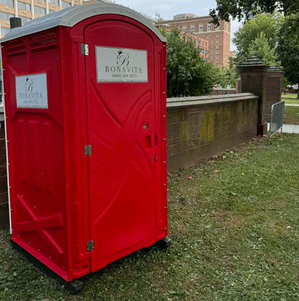 Bonavita portable restroom placed beside a low wall in a city park.