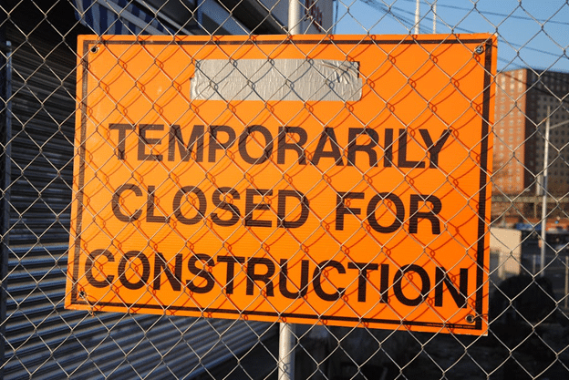 Orange “Temporarily Closed for Construction” sign on chain-link fence.