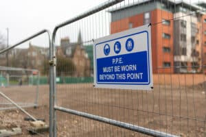 Temporary panel fence with a blue “P.P.E. must be worn beyond this point” safety sign at a jobsite.